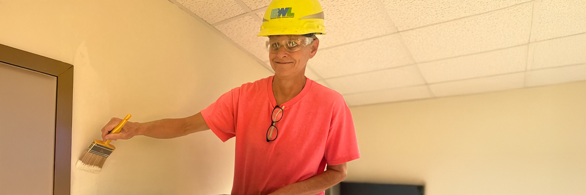 woman in a pink shirt and hard hat painting a wall
