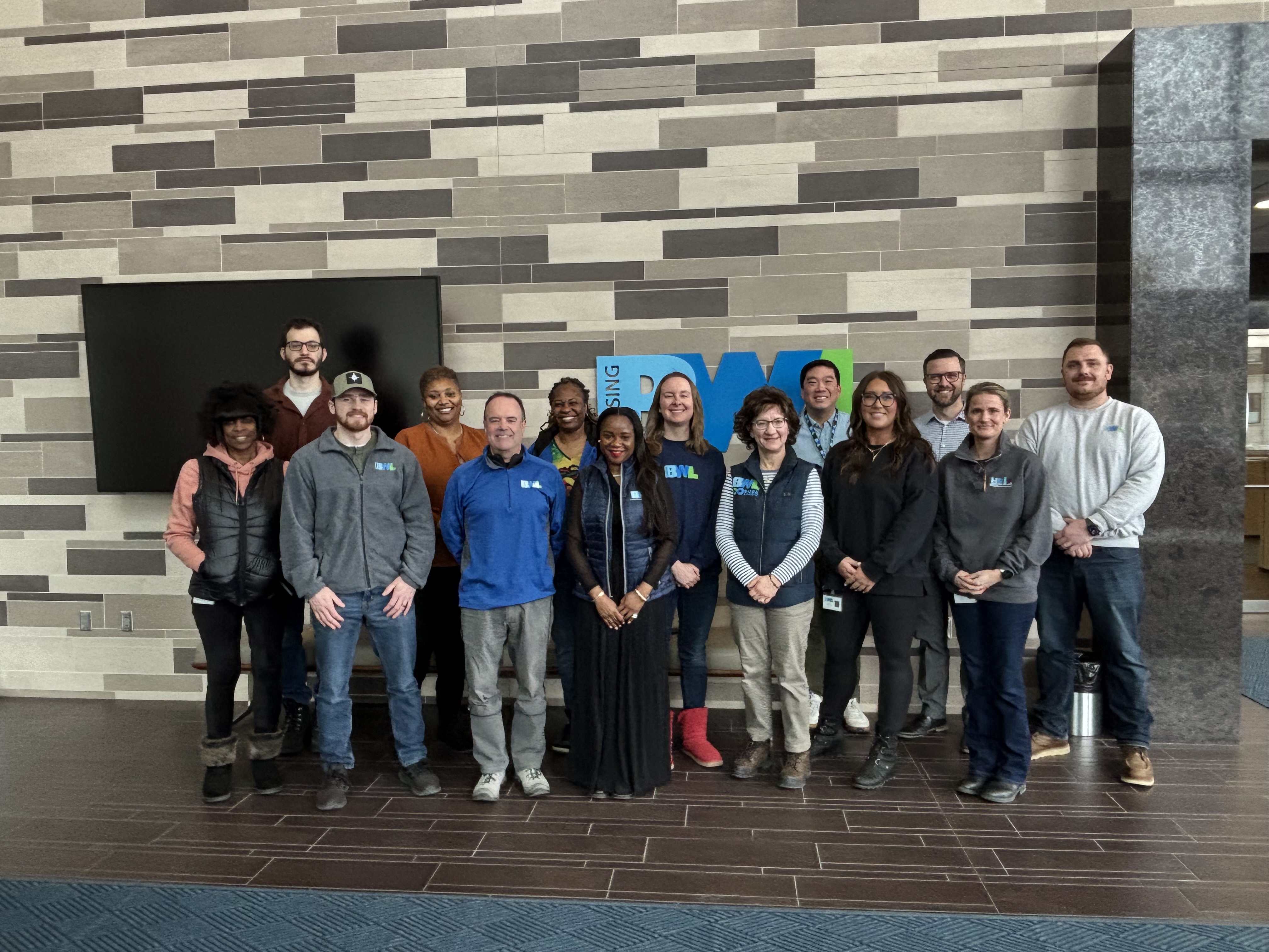big group of people standing in front of brick wall smiling at the camera