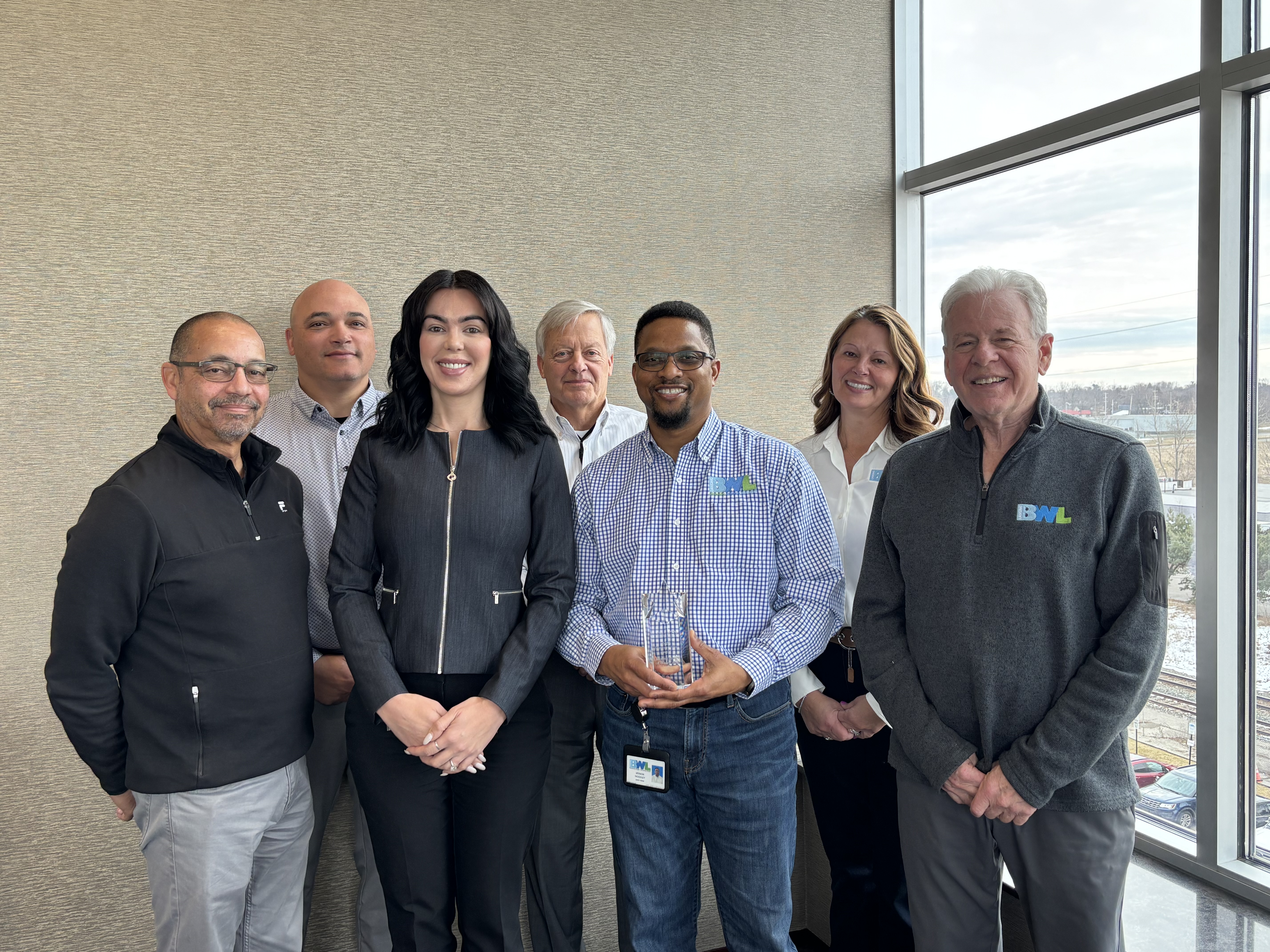 group of 7 people taking a picture with a single award in the middle