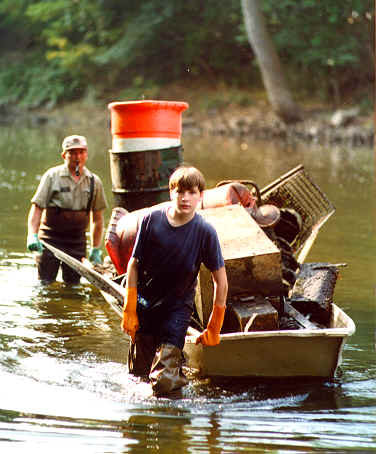 boy in the water pulling a boat full of of trash from the river
