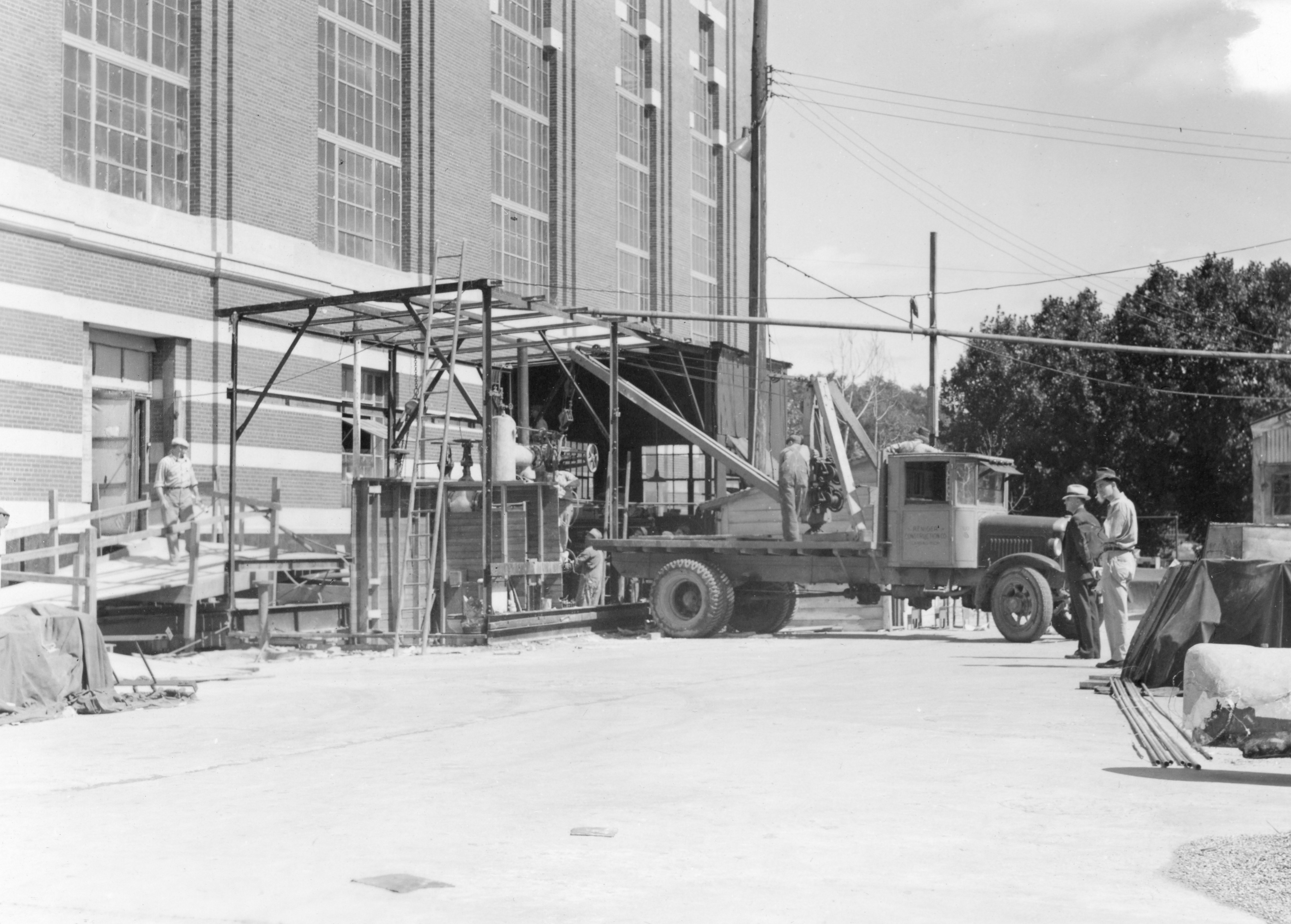a truck parked in front of scaffolding in front of a brick building. With a couple men on the right of the scene looking on.