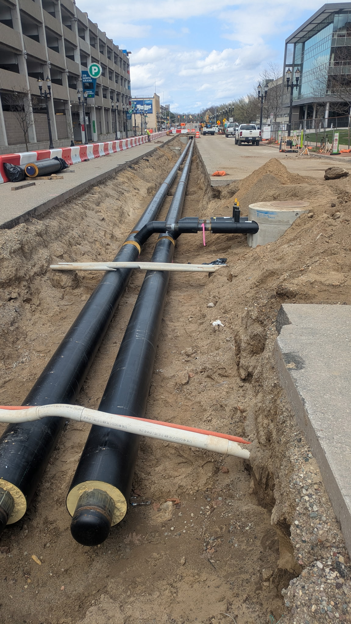 Trench dug in the middle of a road with new black piping place in the bottom of the trench